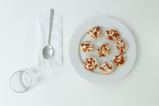 A top view of a white plate of mini pizza bagels on white background