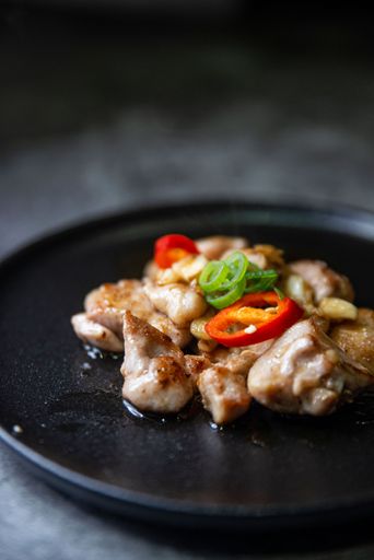 A vertical close-up shot of fried chicken served with colorful peppers on ablack plate