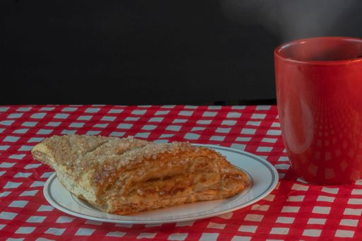 A closeup shot of a plate with a homemade sweet apple turnover pastry near a red cup of tea