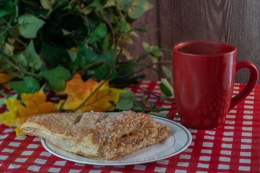 A closeup shot of a plate with a homemade sweet apple turnover pastry near a red cup of tea