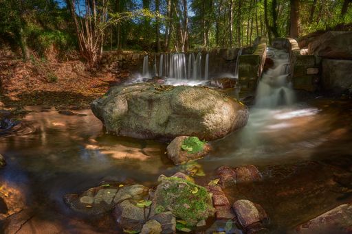 A river with long exposure surrounded by rocks and greenery in a forest under the sunlight