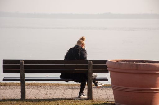 A young female sitting on a wooden bench near the lake