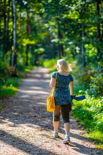A vertical shot of a blonde woman walking on a lovely path in the wild surrounded by lush greenery