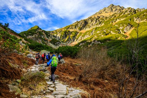 A group of hikers going up a rocky trail surrounded by gorgeous green mountains under a bright blue sky