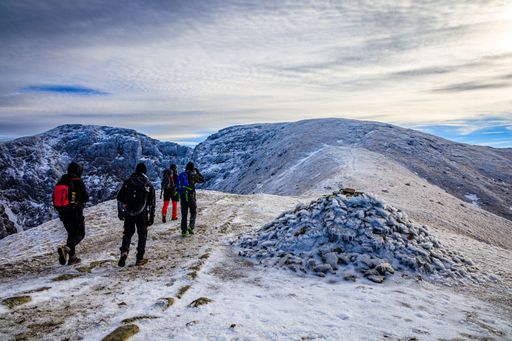 A group of hikers walking along a snow-covered mountain trail towards the mountains range in winter