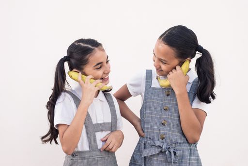 The two Hispanic schoolgirls in uniform imitating phone talking by holding bananas as a telephone