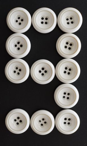 A vertical shot of white buttons assorted like the number nine on a black surface