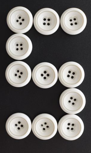 A vertical shot of white buttons assorted like the number five on a black surface