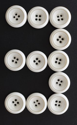 A vertical shot of white buttons assorted like the number three on a black surface