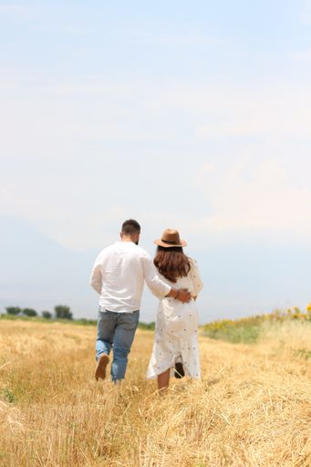 A back view of a romantic young couple walking through a straw field
