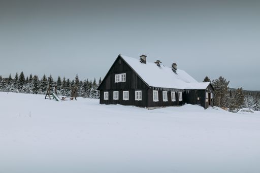 A landscape of a wooden house covered with snow during the winter
