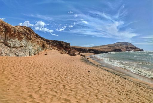 A scenic view of sandy beach and rock formations on the seashore under blue cloudy sky