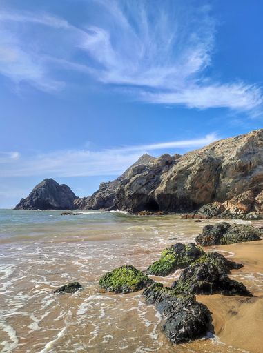 A scenic vertical view of sandy beach and rock formations on the seashore under blue cloudy sky