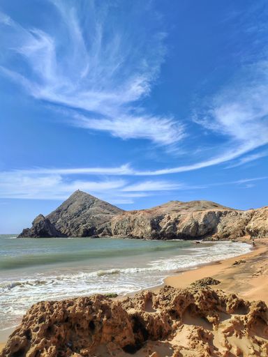 A scenic vertical view of sandy beach and rock formations on the seashore under blue cloudy sky