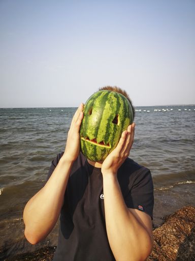 Photo of a young man who cannot be recognized because he is holding a mask carved from a watermelon in front of his face.