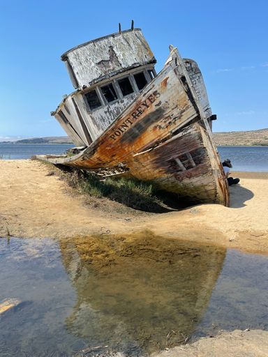 A wooden abandoned fishing boat beached on the sand under blue sky