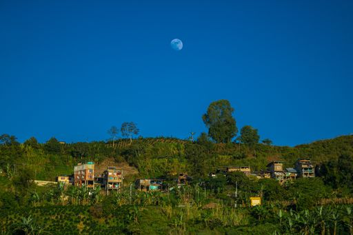 A beautiful shot of a moon seen during day time over a rural housing village