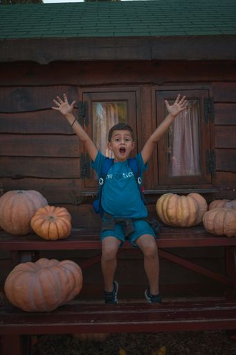 A vertical shot of a young boy in the Halloween park with pumpkins next to him