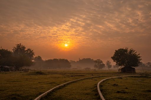 A scenic shot of an empty train railway on a dry field during an orange sunset