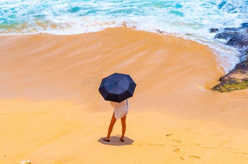 A person standing at the sandy beach with an umbrella in Bali, Indonesia
