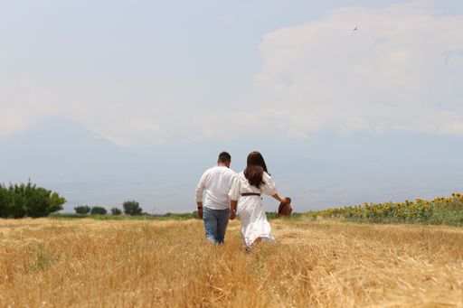 A back view of a young romantic couple holding hands and walking through a straw field
