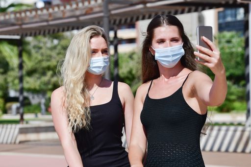 Two young girls wearing surgical masks posing while one of them takes a selfie