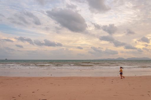 A girl running on a seaside in Thailand, Asia under a cloudy sky at sunset
