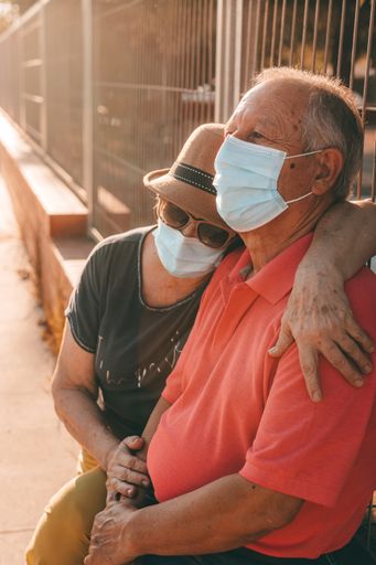 A vertical shot of a mature senior woman hugging her husband while sitting outside during a pandemic