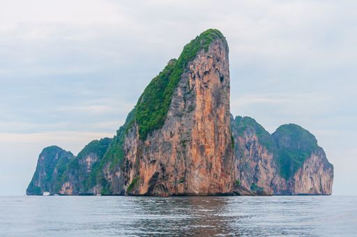 A low angle shot of a rock formation interacting with the clean ocean water in Koh Phi Phi Island, Thailand