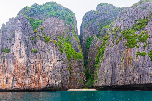 A low angle shot of a rock formation interacting with the clean ocean water in Koh Phi Phi Island, Thailand