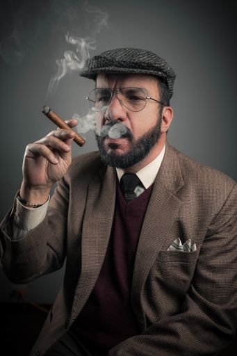 A Hispanic businessman smoking his cigar isolated on gray background