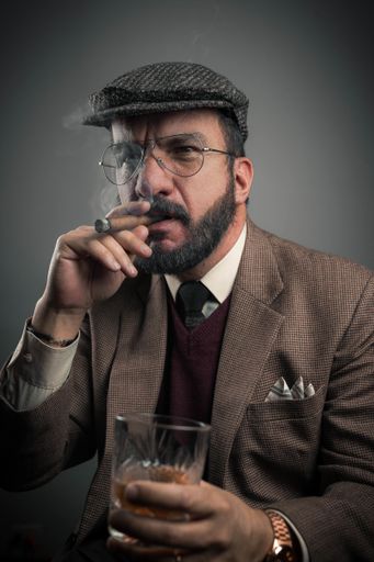 A Hispanic businessman smoking his cigar while holding a glass of whiskey