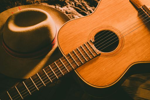 A high angle shot of a brown acoustic guitar near a cowboy hat