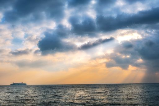 The view of a ship traveling on the horizon under a cloudy sunset sky