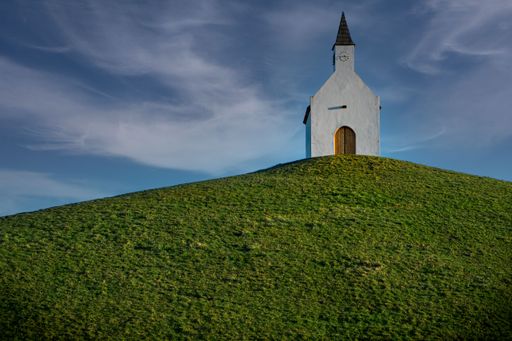 A low angle shot of a small church on a rural green hill in the Netherlands