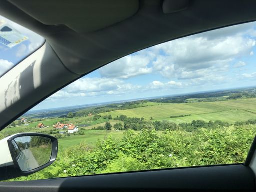 a view to the green field under the clouds form the right side rear window of the car