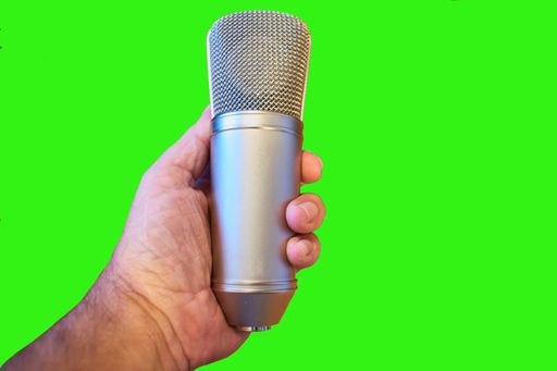 An isolated closeup of a man's hand holding a condenser microphone on a green background