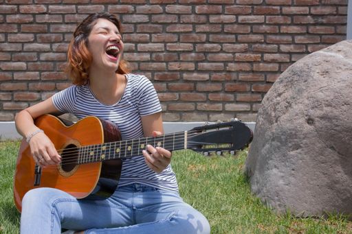 A beautiful Hispanic young woman playing her guitar against a brick wall background