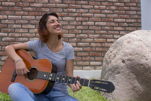 A beautiful Hispanic young woman playing her guitar against a brick wall background
