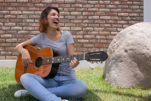A beautiful Hispanic young woman playing her guitar against a brick wall background
