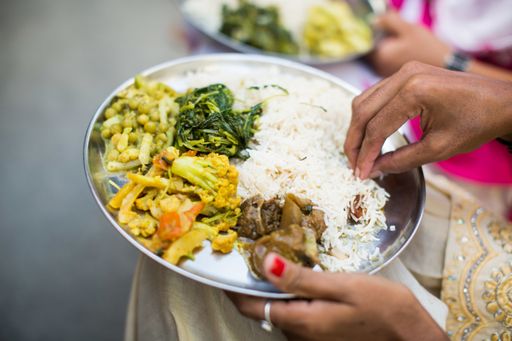 An Indian female eating traditional dish with rice, peas, meat and vegetables in a silver tray