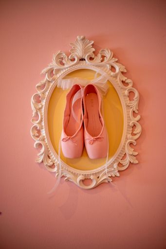A pink ballerina shoes hanging on a mirror frame isolated on a pink background