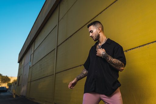 A young hot man wearing a black oversize shirt and pink pants standing against a bright yellow wall