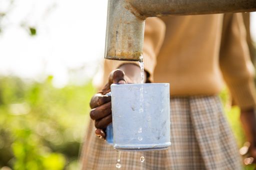 An African female filling water in a blue metal mug from a rusty sink in a poor village - poverty concept