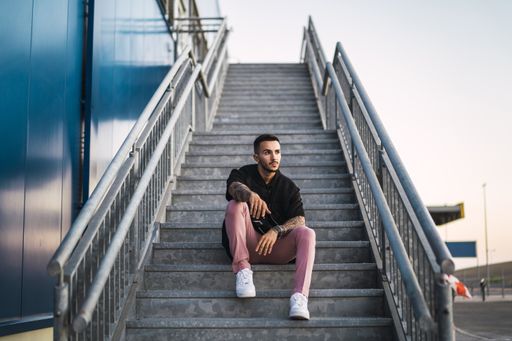 A young hot man wearing a black oversize shirt and pink pants sitting on a staircase