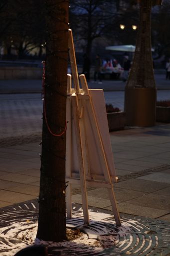A vertical shot of wooden easel stand leaning on a tree in the park