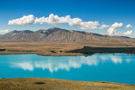 A beautiful rocky mountain on the shore near the lake with fluffy clouds reflecting in the lake
