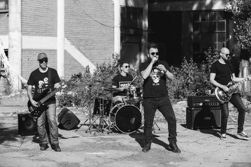A grayscale shot of a male rock band performing on the street during a sunny day