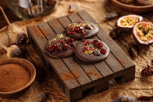 A closeup shot of dark chocolate cookies on a small wooden pallet, surrounded with cocoa powder