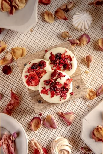 A top view vertical shot of white handmade chocolates with red filling, surrounded with petals on the table